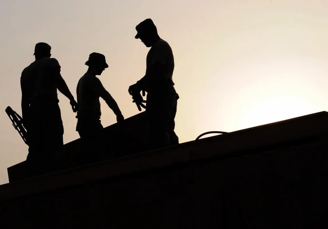 Silhouetted workers on rooftop at sunset